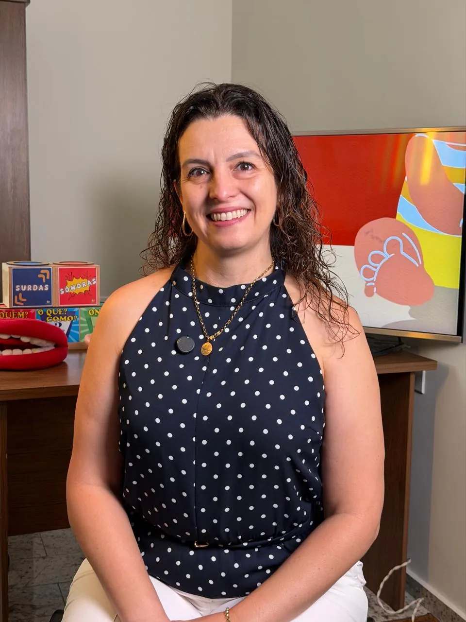 Rosane no consultório, com materiais de terapia na mesa ao fundo